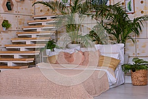 Beautiful bedroom interior with large bed, pillows, wooden stairs and shelves, plants
