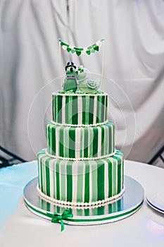 Beautiful big three leveled wedding cake decorated with two birds on the top. A green-white striped wedding cake with