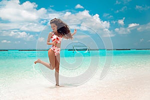 Beautiful bikini Woman with long hair jumping on tropical beach. Pretty slim girl posing on exotic island in turquoise ocean.