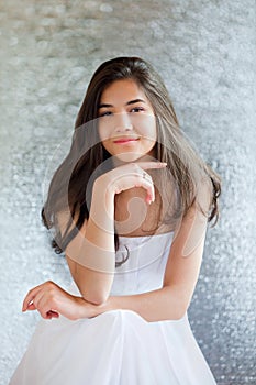 Beautiful biracial teen girl in white dress sitting, thinking