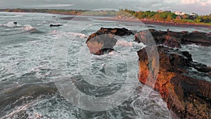 A beautiful bird's-eye view of flying around the black rocks on ocean at the golden hour. Drone shots of the