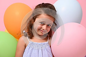 Beautiful birthday 4 years girl smiling looking at camera, standing behind multicolored balloons , isolated over pink background,