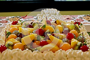 Beautiful birthday creamy cake with many fruit on top.