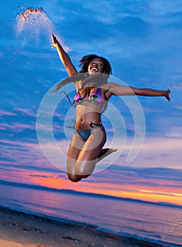 Beautiful black African American woman jumping on the beach at s