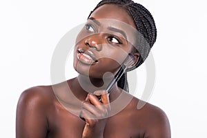 Beautiful black african model with flawless complexion and smooth skin holding a make up brush against her cheek isolated on white