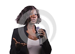 Beautiful black afro American business woman with microphone speaking in auditorium at corporate event or seminar giving