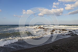 Beautiful black beach with coast and sea in Vlichada with blue sky background with white clouds and sea