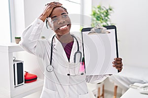 Beautiful black doctor woman holding clipboard stressed and frustrated with hand on head, surprised and angry face