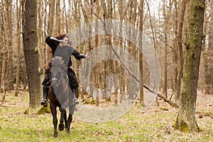 Beautiful black dressed woman in historical costume with bow and arrow shoots from a bow before riding a horse