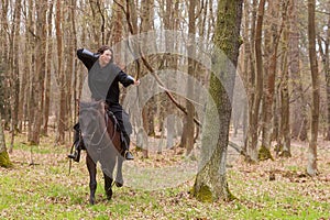 Beautiful black dressed woman in historical costume fired an arrow from a bow while riding a horse