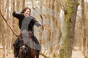 Beautiful black dressed woman in historical costume with shoots from a bow before riding a horse