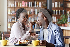 Beautiful black girl feeding yummy pie to her boyfriend at cozy cafe