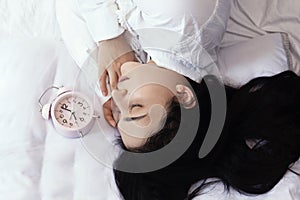 Beautiful black-haired woman sleeping in cozy bed. The alarm clock set at 7 a.m. morning. Female is going to wake up at 7 o`clock