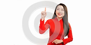 Beautiful black-haired young woman in ao dai standing on a white background with a bright smile on her lips, pointing her finger a