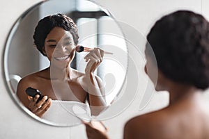 Beautiful black lady applying makeup in bathroom