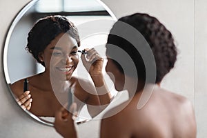 Beautiful black lady applying makeup in bathroom, using mascara