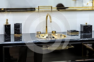 A beautiful black marble washbasin with a gold tap and fittings. Gold sink, led mirror, marble black dispensers