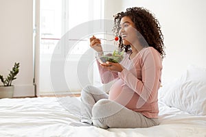 Beautiful black pregnant woman with radiant smile eating fresh vegetable salad