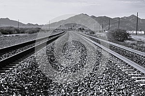 Beautiful black and white shot of railroads and soil road next to high mountains