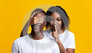 Beautiful black woman covering man eyes, showing silence gesture