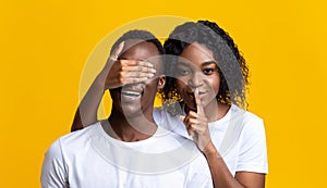 Beautiful black woman covering man eyes, showing silence gesture photo