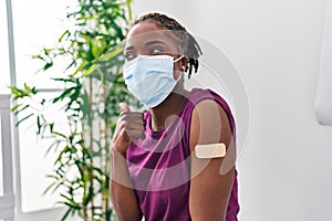 Beautiful black woman getting vaccine showing arm with band aid pointing thumb up to the side smiling happy with open mouth