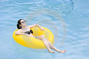 Beautiful black woman with glass of summer cocktail on inflatable ring at pool