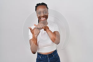 Beautiful black woman standing over isolated background pointing to the back behind with hand and thumbs up, smiling confident