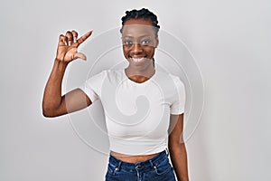 Beautiful black woman standing over isolated background smiling and confident gesturing with hand doing small size sign with