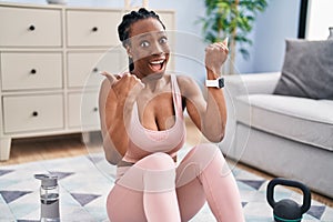 Beautiful black woman using smart watch training at home pointing thumb up to the side smiling happy with open mouth