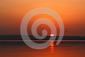 Beautiful blazing sunset landscape at the river Dnipro and orange sky above it with awesome sun golden reflection on calm water