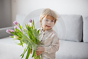 Beautiful blond boy, giving mother flowers and box with little gift for mothers day