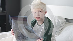 A beautiful blond boy is studying a picture of his lungs in the hospital.