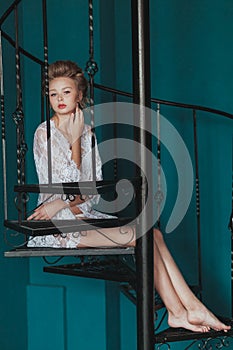 Beautiful blond bride in white negligee sitting on the black wrought iron stairs.