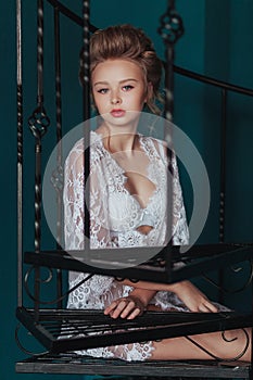 Beautiful blond bride in white negligee sitting on the black wrought iron stairs.