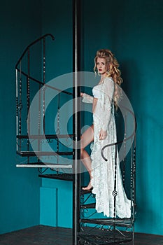 Beautiful blond bride in white negligee walking up black wrought iron staircase
