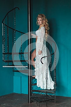 Beautiful blond bride in white negligee walking up black wrought iron staircase