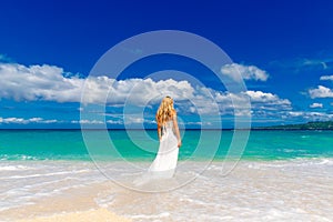 beautiful blond fiancee in white wedding dress with big long white train stand on shore sea
