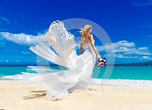 beautiful blond fiancee in white wedding dress with big long white train and with wedding bouquet stand on shore sea