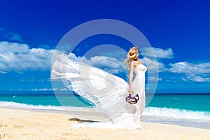 beautiful blond fiancee in white wedding dress with big long white train and with wedding bouquet stand on shore sea