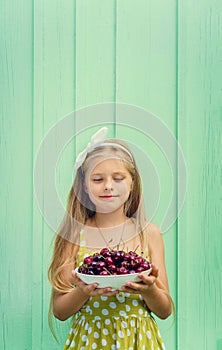 Beautiful blond girl on a background of turquoise wall holding plate with cherry.