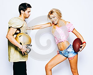 Beautiful blond girl cheerleader with a ball is attacking a quarterback. A player in a football uniform with a helmet