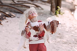 Beautiful blond girl child hugs and plays with a dog on the beach in summer, enjoying outdoor fun and affectionate