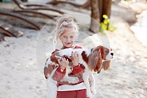 Beautiful blond girl child hugs and plays with a dog on the beach in summer, enjoying outdoor fun and affectionate