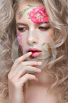 Beautiful blond girl with curls and a floral pattern on the face. Beauty flowers.