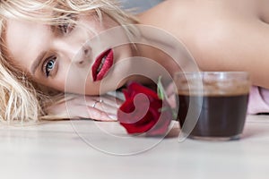 Beautiful blond girl lies on the floor with a cup of hot morning coffee and a bouquet of roses