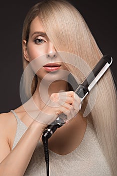 Beautiful blond girl with a perfectly smooth hair, classic make-up with curling styler in the hands.