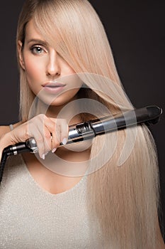 Beautiful blond girl with a perfectly smooth hair, classic make-up with curling styler in the hands.