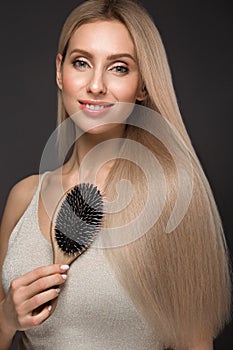 Beautiful blond girl with a perfectly smooth hair, classic make-up with hairbrush in the hands. Beauty face.