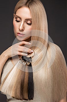 Beautiful blond girl with a perfectly smooth hair, classic make-up with a palette for hair extensions in the hands photo